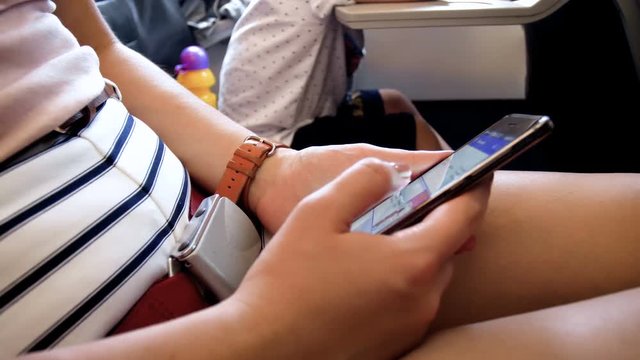 Closeup 4k video of young woman browsing internet via wi-fi on smartphone during flight in airplane