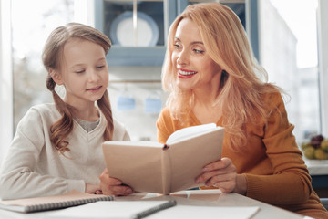 Keep smiling. Cheerful female person expressing positivity while doing homework with her daughter