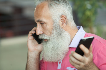Emotional portrait of a cheerful and stylish mature business man with a bald head , with a smile talking on the smartphone with a friend. Bearded Senior man