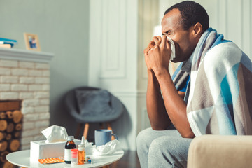 Running nose. Displeased afro american man using tissue and sitting