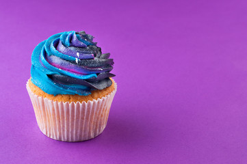 Cupcake with galaxy dark whipped cream on violet background