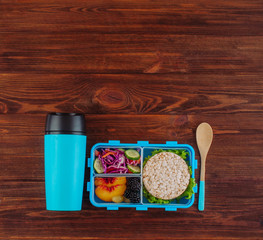 Open lunch box with thermos mug on rustic wooden background