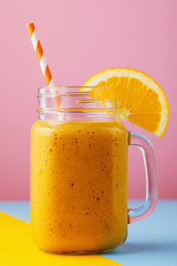 Smoothies of ripe orange in a glass jar with fruit on a colored background