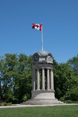 Canadian Flag Waving On The Top Of A Clock And Bell Tower In A Park With Trees In The Background