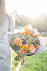 Bird of paradise flower, beautiful spring bouquet. Young girl holding a flower arrangement with variety of colors. Violet, blue and peach color flower. Bright dawn or sunset sun