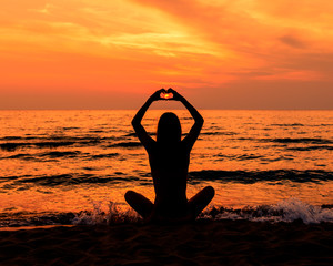 Teen Girl In A Bathing Suit With Long Hair At The Beach In Silhouette During Sunset Making A Heart With Her Hands