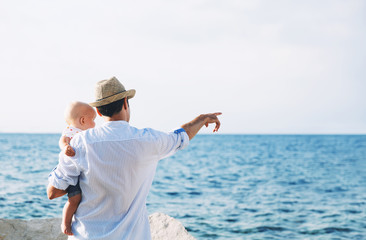 Father and baby are point out on sea and sky backgrounds.