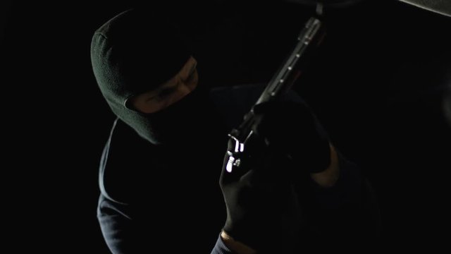 Serial killer in face mask opening car trunk and taking pistol, contract crime