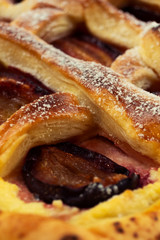 Baking puff pastry with baked plums stacked in the cells of the pie, close-up, vertical frame.