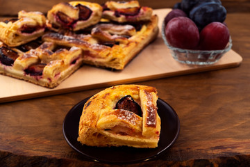Cut off piece of baked cake with plums and cottage cheese on a round plate, wooden background.