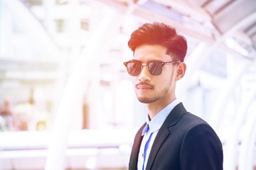 Young businessman wear suit and sunglass is standing on city background