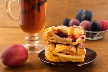 Breakfast of pieces of plum cake and mint tea, wooden background.