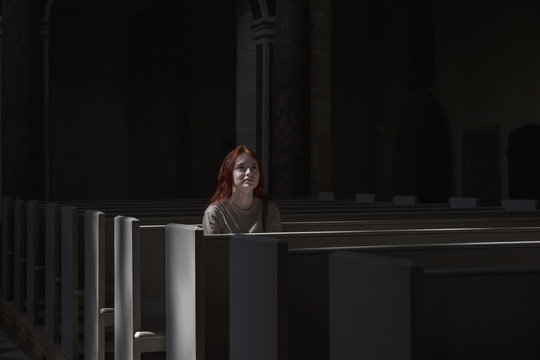 Young beautiful red-haired girl lonely sits in church praying to God with faith looking forward.