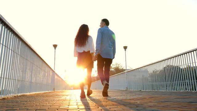 Young couple of man and woman walking on bridge at summertime. Sunset light. Stylish happy pair in business clothes holding hands on date through empty street. 4k.