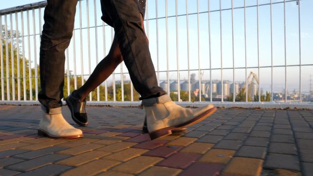 Legs of unrecognizable young couple walking on bridge at summertime. Sunset light. Stylish happy pair in business clothes holding hands on date through empty street. 4k