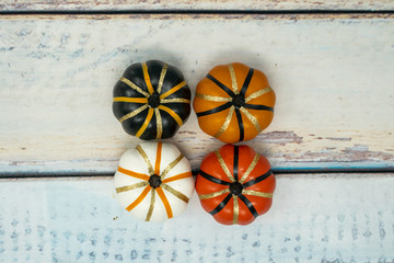 Four decorative fake pumpkins (white, orange and black) with gold glitter details arranged on a blue wooden background. Concept for autumn scene