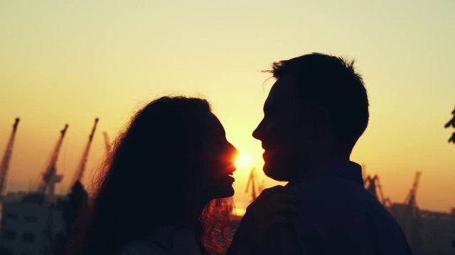 Silhouette of happy couple spending intimate time together at autumn park. Sunset light, sun flares. Lovers enjoying on date. Girl and man hugs, smiling. Love, family, care concept.