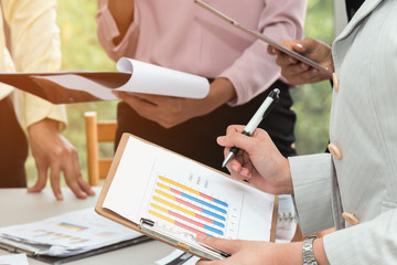 Business woman holding clipboard with the document paper has a graph showing earnings data and pen in hand,Young business people group are meeting to discussion on a business deal,Business concept.
