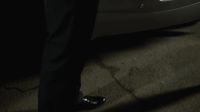 Male criminal paying kidnapper for tied female victim lying in auto trunk