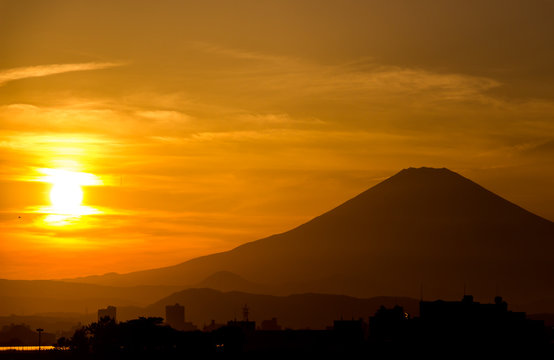 A golden sun setting beside the silhouette of mount Fuji