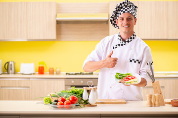 Young professional cook preparing salad at kitchen