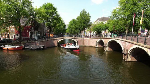 A nice summer day on Amsterdam canals with traditional boat, old houses and bridge  in Netherlands