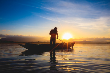 Fototapeta premium Silhouette fisherman standing in the boat during sunrise