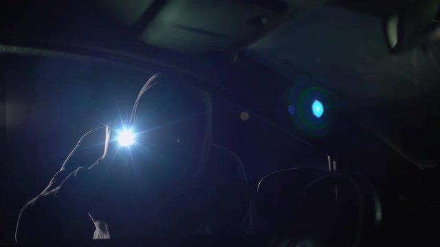 Criminal in balaclava with flashlight looking inside car, robbery, carjacking