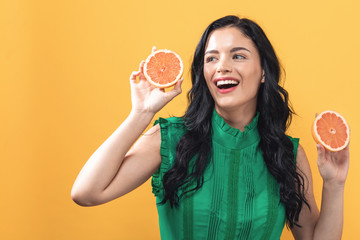 Happy young woman holding oranges on a yellow background