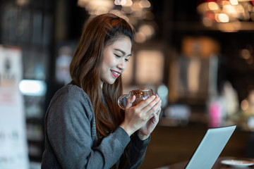 Beautiful Attractive Asian Business woman smile and holding coffee in Coffee shop cafe with computer laptop on the table feeling so happiness and comfortable