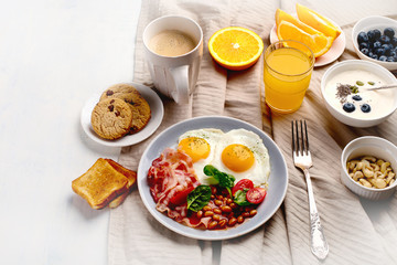 Breakfast with fried eggs, bacon, orange juice, yogurt and toasts