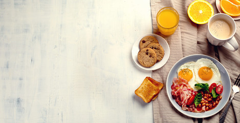 Breakfast with fried eggs, bacon, orange juice, yogurt and toasts