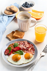 Breakfast with fried eggs, bacon, orange juice, yogurt and toasts