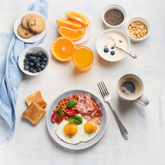 Breakfast with fried eggs, bacon, orange juice, yogurt and toasts