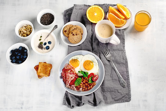 Breakfast with fried eggs, bacon, orange juice, yogurt and toasts