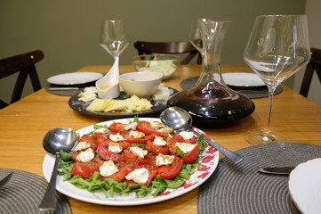 A table with snacks/with sliced cheeses. On the table there is a decanter with wine and stemware.