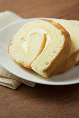 Slices of vanilla roll cake in white plate on wooden table.