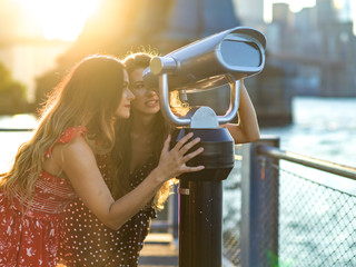 Two women looking into binocular by river