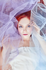 Redhead Girl dreams, bright makeup, clean skin, facial care. Redhead girl in a light air colored dress lies on the floor, a portrait close-up. Romantic woman with long hair and cloud dress