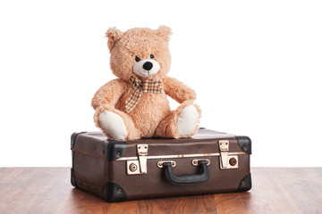 Old teddybear sitting on vintage suitcase