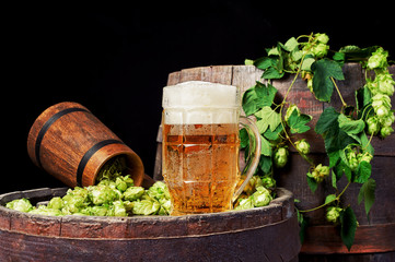 A mug of beer and hops on an old barrel .