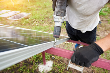 Close-up angled view of technician working with screwdriver connecting solar photo voltaic panel to exterior metal platform. Alternative renewable ecological green sun energy sources concept.
