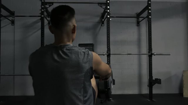 Young Fit Tanned Man Working Out on Rowing Machine at Gym Rear View