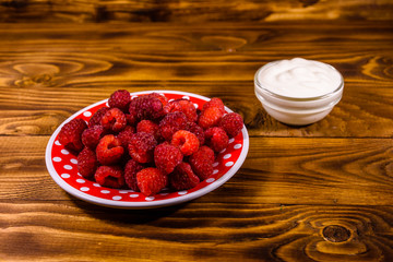 Ceramic plate with ripe raspberries and sour cream on wooden table