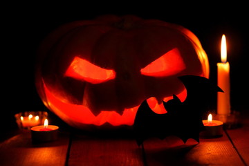 Pumpkin on Halloween. Candles, bat and glowing pumpkin. Harvest for Halloween. Dark atmosphere for holiday. Kazhan and light of candles. Pumpkin on wooden boards