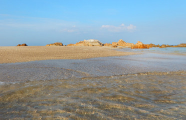 Underwater view of pebble on sea bottom and wave on water surface on blue sky background.