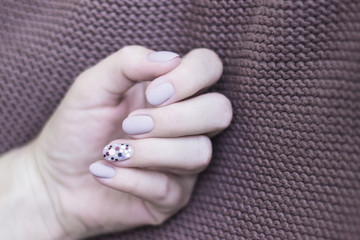 manicure nails art design gray beige color matte nail polish with sequins of black, brown, silver on a brown knitted background