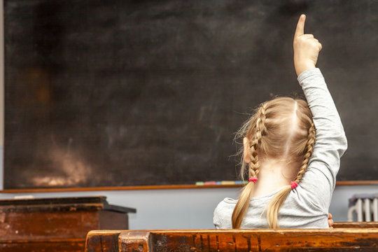 Concept of public primary school education with young girl raising her hand in the classroom