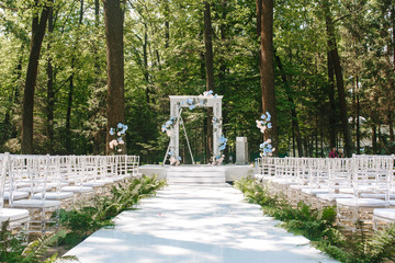 A flower wedding arc stands in the nature in a park on a sunny day. Front view with chairs