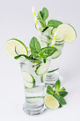 Cold spring drink with cucumber, lime, mint and ice on soft white background.